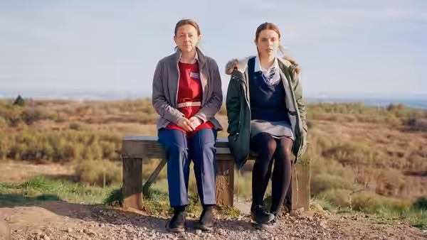 Bethan (Gabrielle Creevy) sits beside an older woman on a bench overlooking the countryside