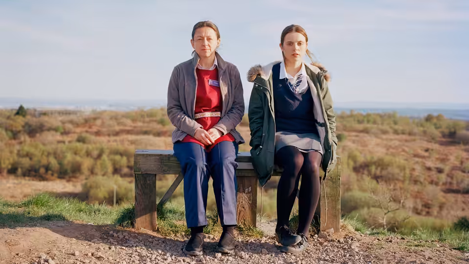 Bethan (Gabrielle Creevy) sits beside an older woman on a bench overlooking the countryside