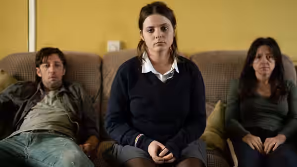 Bethan sits between a man and a woman on a living room sofa