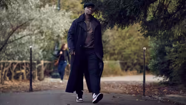 Assane Diop (Omar Sy) walks along a tree-lined path in a long dark coat