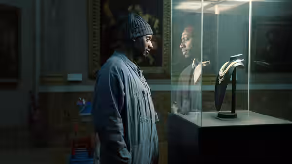 A bearded man in a knit cap studies a necklace inside a glass display case