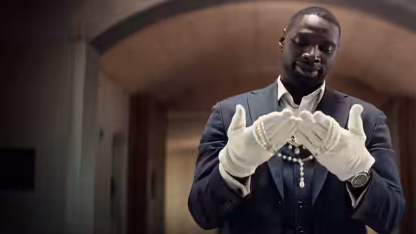 Assane Diop (Omar Sy), dressed as a museum attendant, examines his white gloves indoors