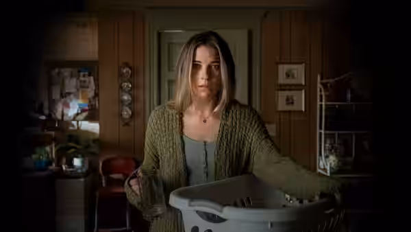 Allison McRoberts (Annie Murphy) stands holding a laundry basket in a wood-paneled home