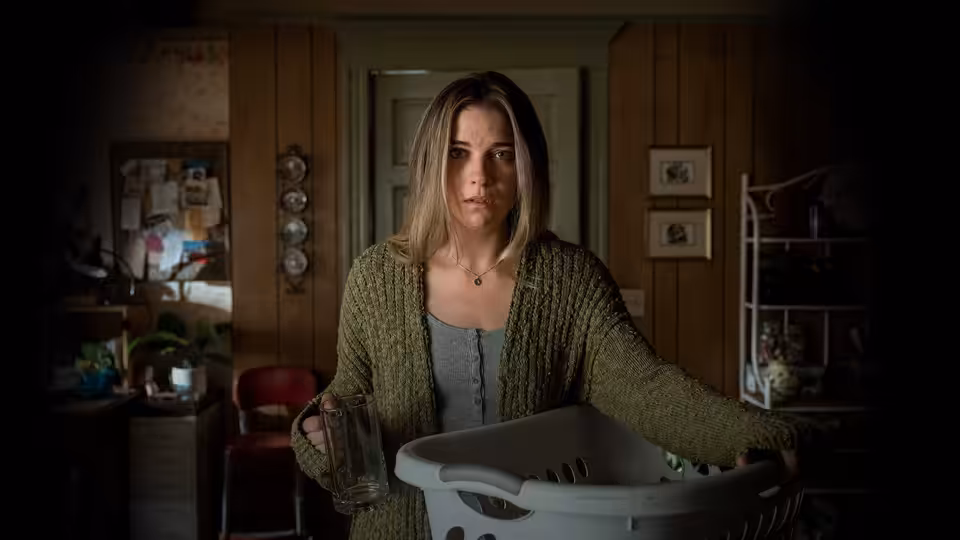 Allison McRoberts (Annie Murphy) stands holding a laundry basket in a wood-paneled home