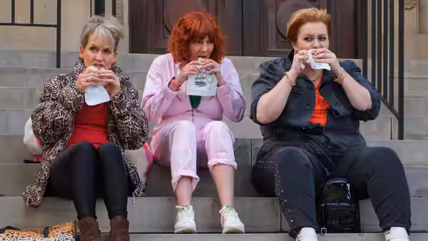 Alma and two women eat together on outdoor steps