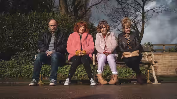 Alma sits with three people on a bench in a park