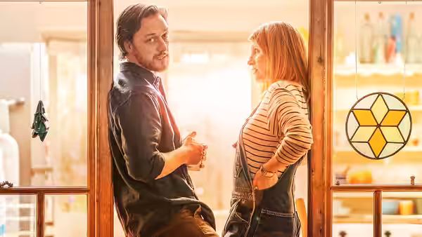 He (James McAvoy) leans in a doorway holding a glass as She (Sharon Horgan) faces him