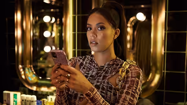 A woman in a patterned outfit checks her phone in a mirrored interior