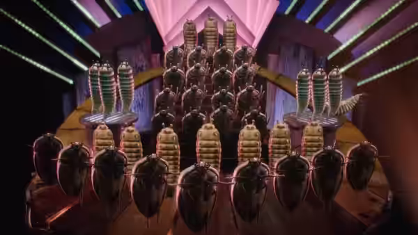 Rows of cockroaches perform on a brightly lit stage