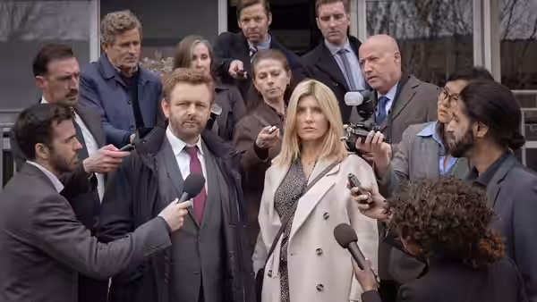 A woman and man face reporters and microphones outside a building