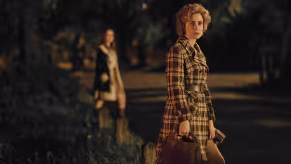 A curly-haired woman carrying a handbag turns toward the camera while another woman walks behind her