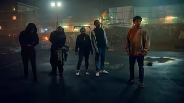 Five young people stand scattered across a floodlit outdoor court