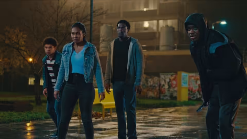 Four young people gather on a rain-soaked courtyard at night
