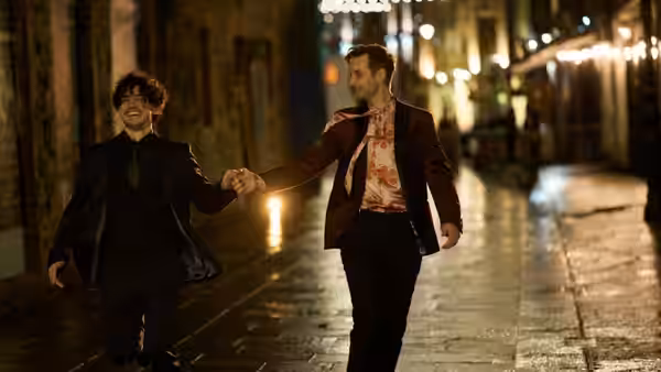 Two men walk hand in hand along a wet, lantern-lit street