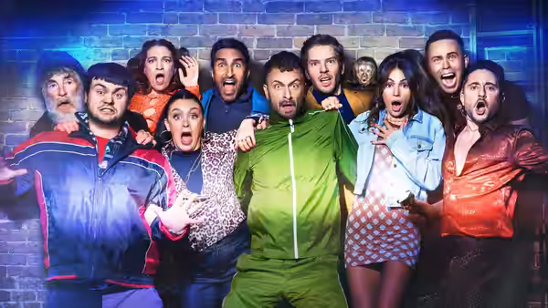 A group of people react together against a blue-lit brick wall