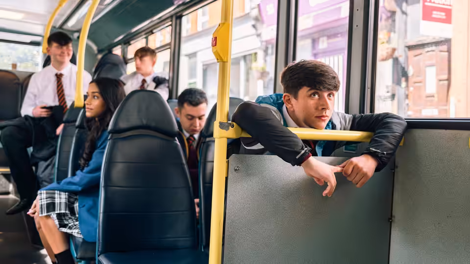 A schoolboy leans over a partition on a bus as classmates sit behind him