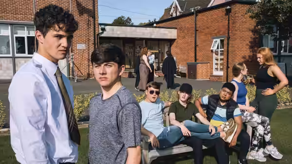 Teenagers gather outside a school building as two boys stand in the foreground