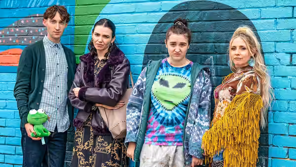 Chi stands with three companions against a painted brick wall