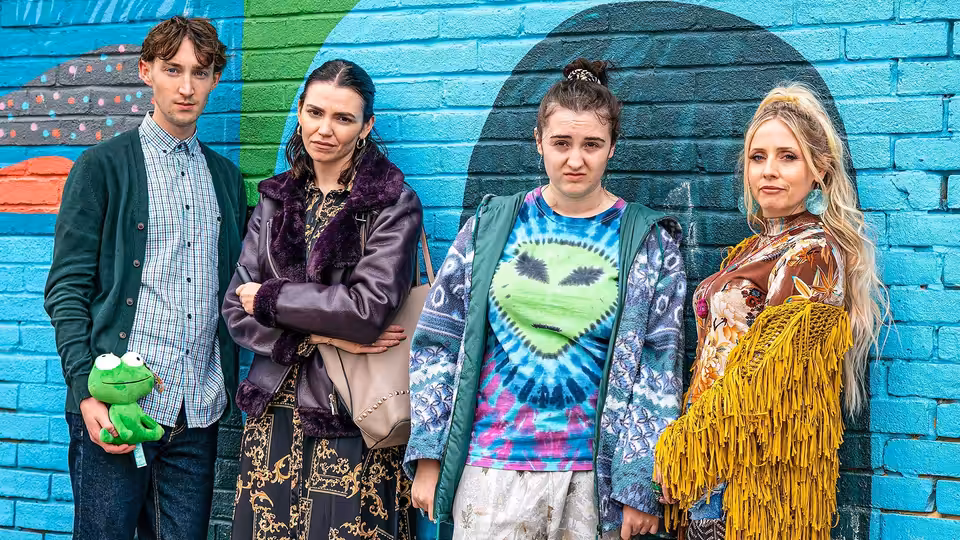 Chi stands with three companions against a painted brick wall