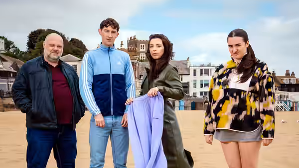Chi and three companions stand on a beach beside a lavender garment