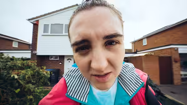 Chi leans close to the camera outside a suburban house