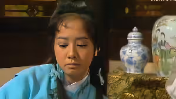 A young person in turquoise robes looks down beside ornate porcelain jars