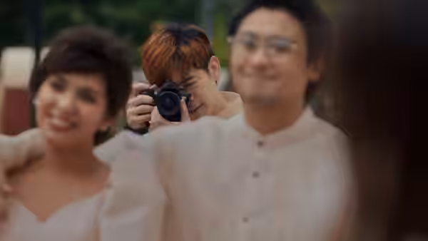 Apollo (Joshua Garcia) photographs a smiling bride and groom outdoors