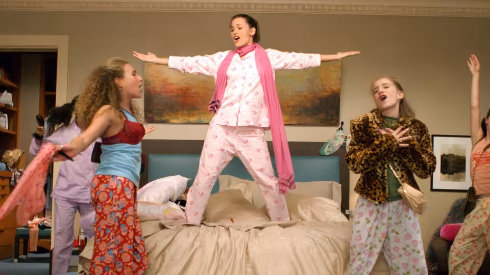 Jenna (Jennifer Garner) stands on a bed with arms outstretched as friends dance around her