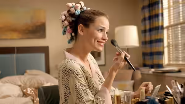 Jenna (Jennifer Garner) applies makeup at her vanity with curlers in her hair