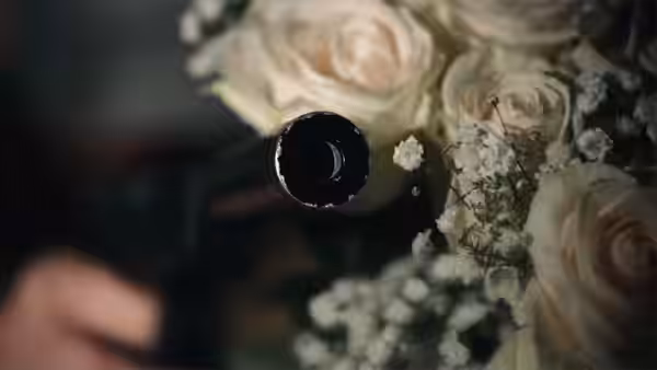 A dark gun barrel points past a bouquet of white roses toward a blurred man