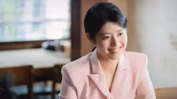 A smiling woman in a pink blazer sits at a table