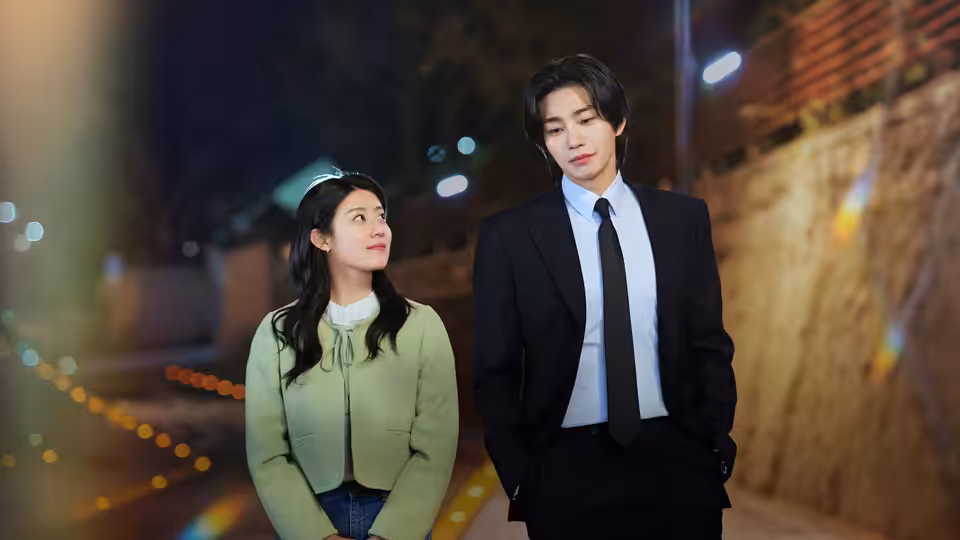 A woman and a suited man walk together along a brick-lined street at night