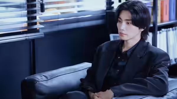 A man in a black suit sits on a leather sofa in an office