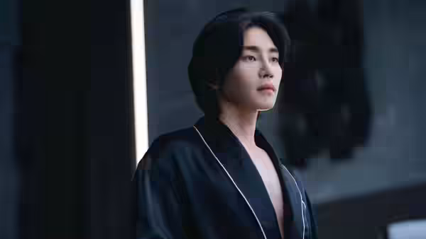 A man in a dark robe stands beside a wall in a dim room