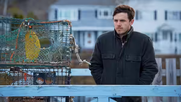 Lee Chandler (Casey Affleck) standing on a dock beside a lobster trap