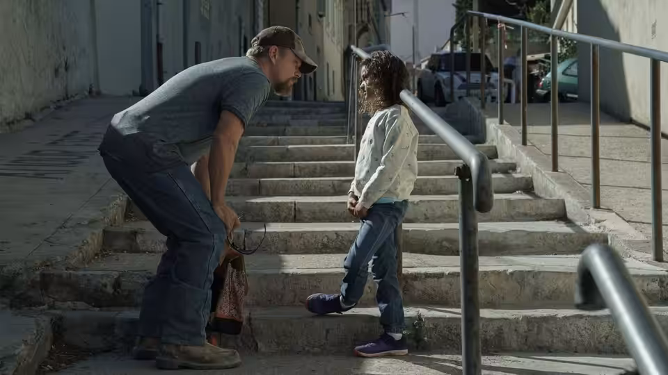 Bill Baker (Matt Damon) crouches beside Maya on a stone staircase
