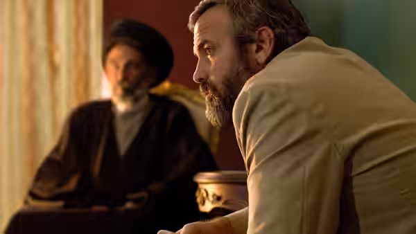 Bob Barnes (George Clooney) leans forward beside a seated cleric