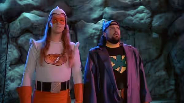 Jay and Silent Bob stand in superhero costumes inside a rocky cavern