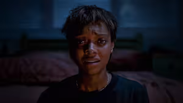A distressed woman with red eyes stares forward in a bedroom