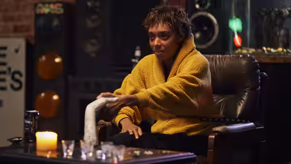 A woman in a yellow robe reaches forward from a leather chair