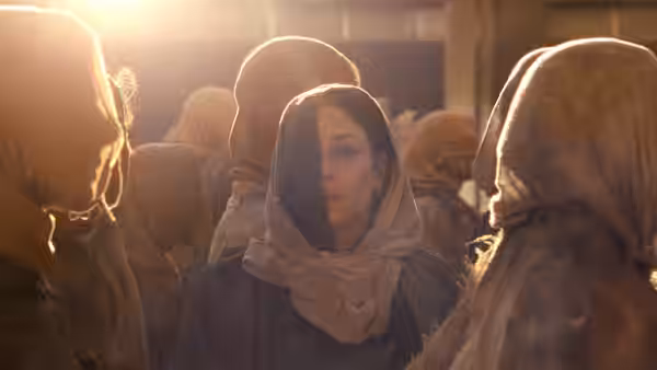 Rana (Noomi Rapace) in a headscarf stands among a crowd of hooded people