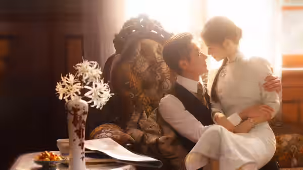A seated man holds a woman in white beside a sunlit window