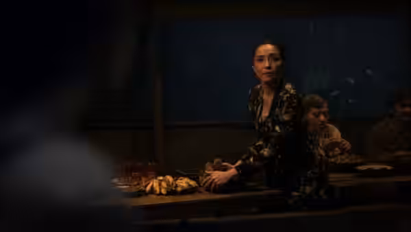 A woman seated at a wooden table turns toward someone nearby