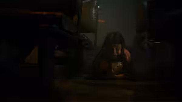 A young girl crouches beneath a bed beside a doll