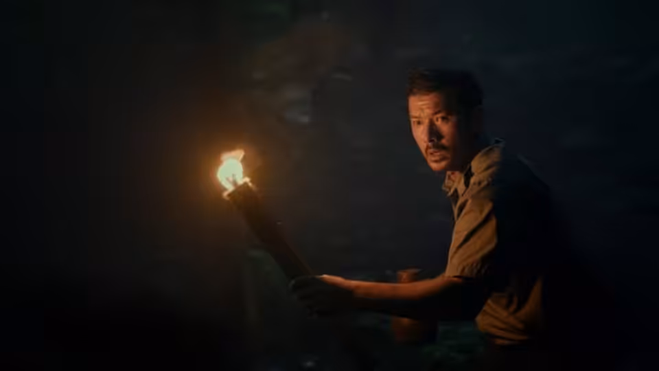 A man crouches in darkness, holding up a burning torch