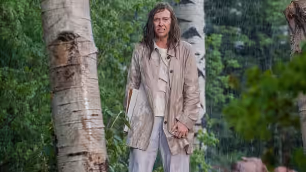 a long-haired man standing in the rain among birch trees