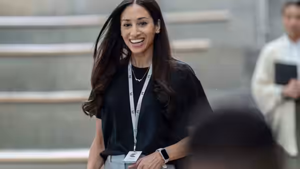 A smiling woman wearing an identification badge stands in a bright hallway