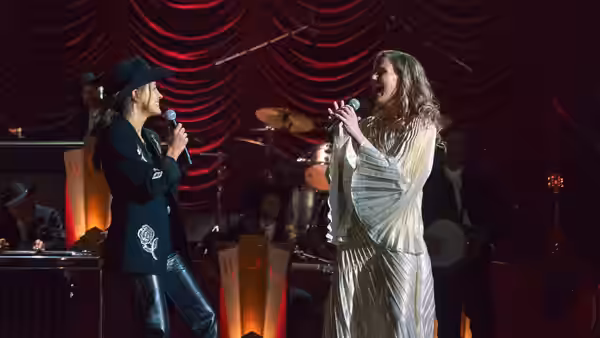 Two women sing to each other onstage as a band plays behind them