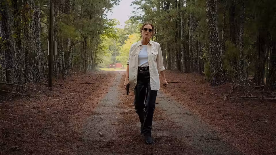 A woman in sunglasses walks along a dirt path through a wooded area
