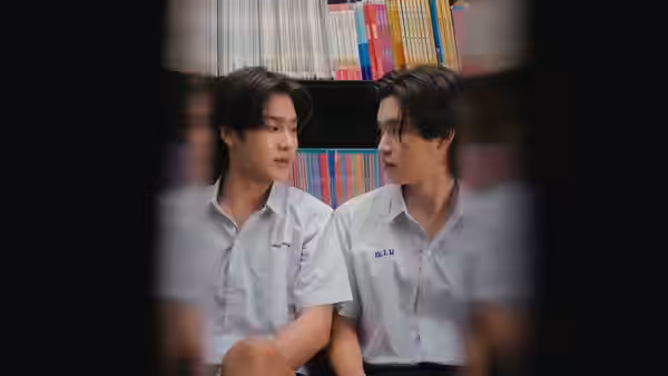 Two schoolboys sit beside a bookshelf, turning to talk with each other
